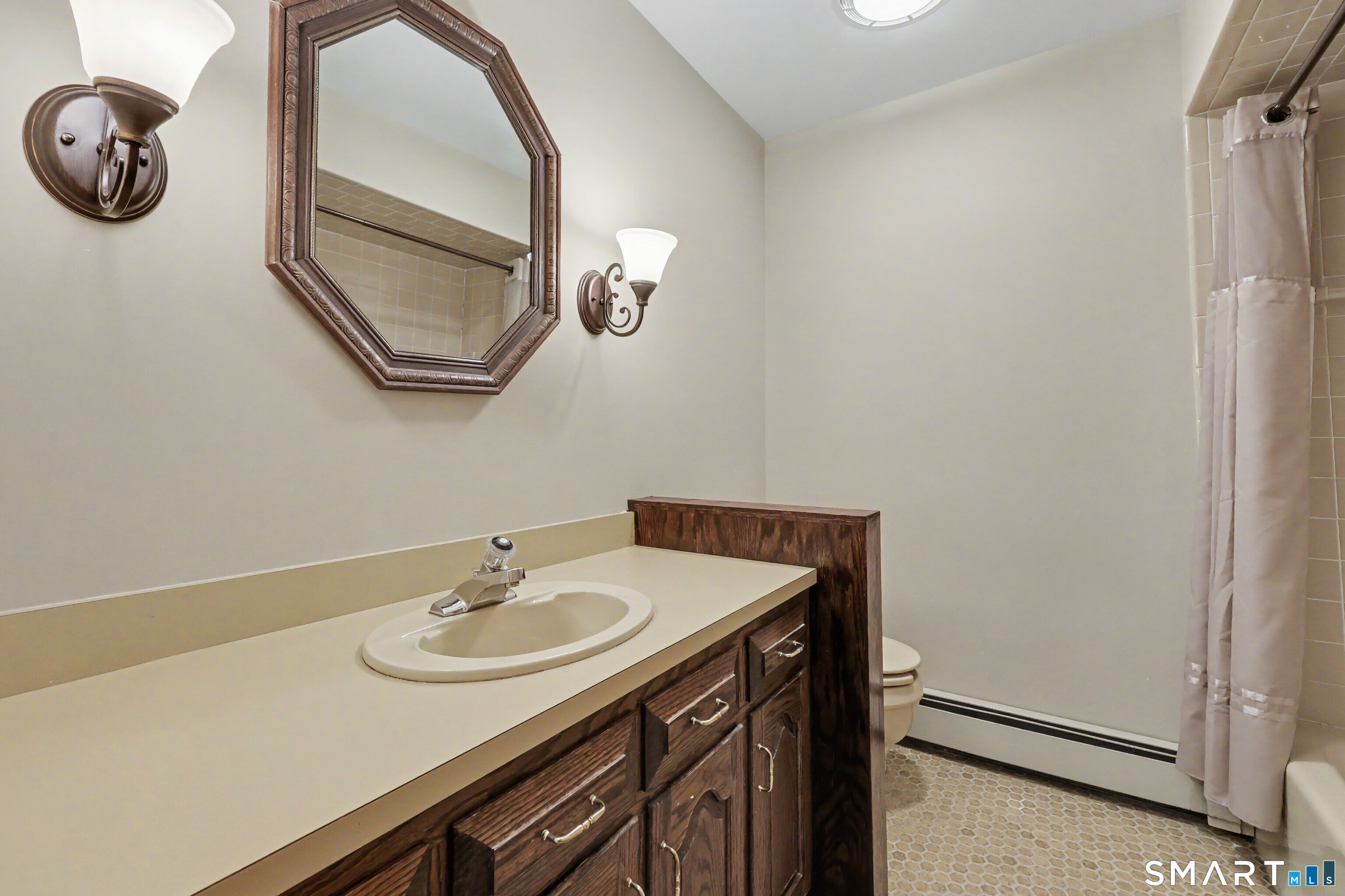 Bathroom with a dark wood vanity, cream countertop, ornate octagonal mirror, and curtained tub or shower.