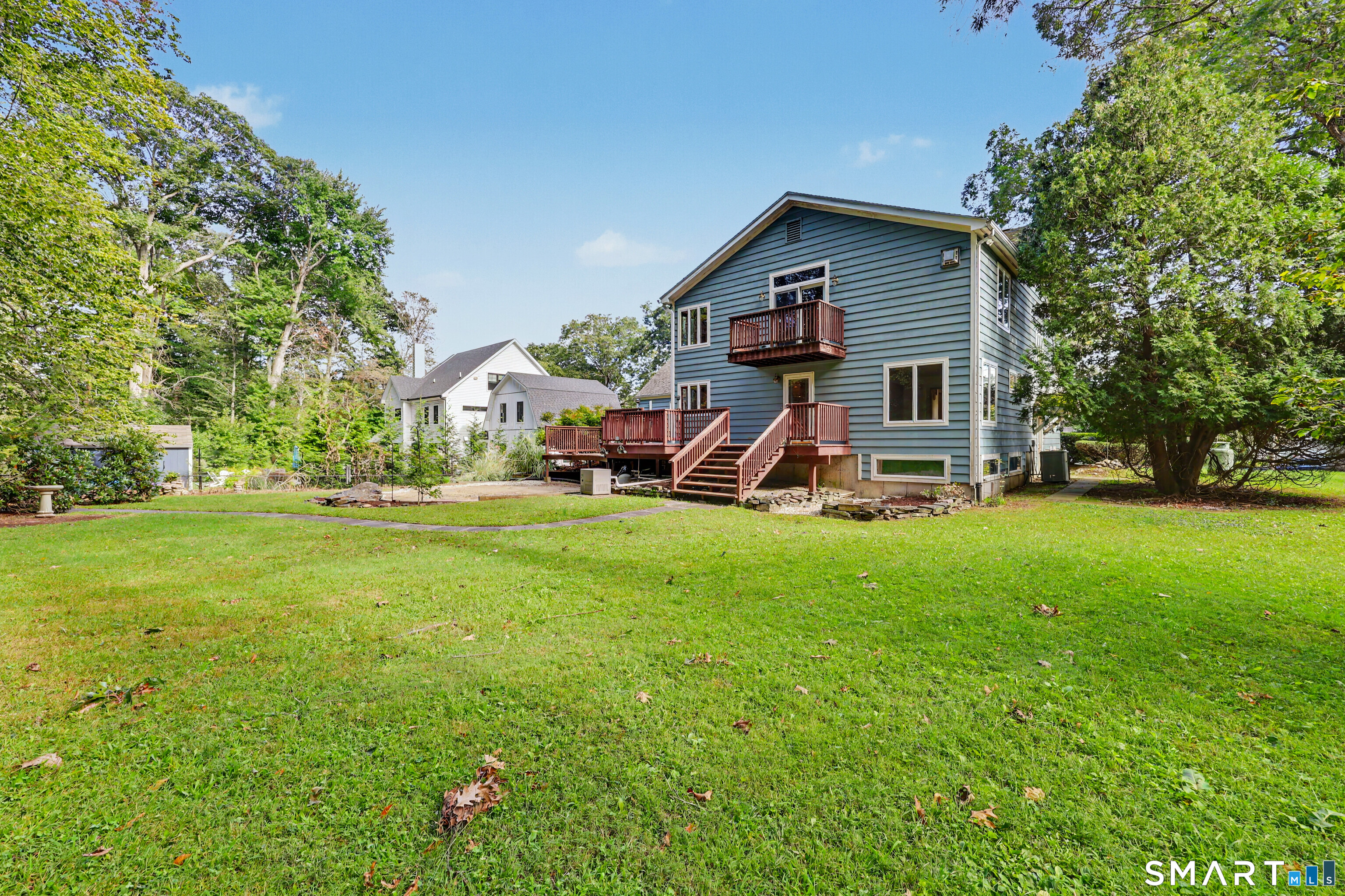Blue-sided house with multiple wooden decks overlooking a broad lawn and mature trees.