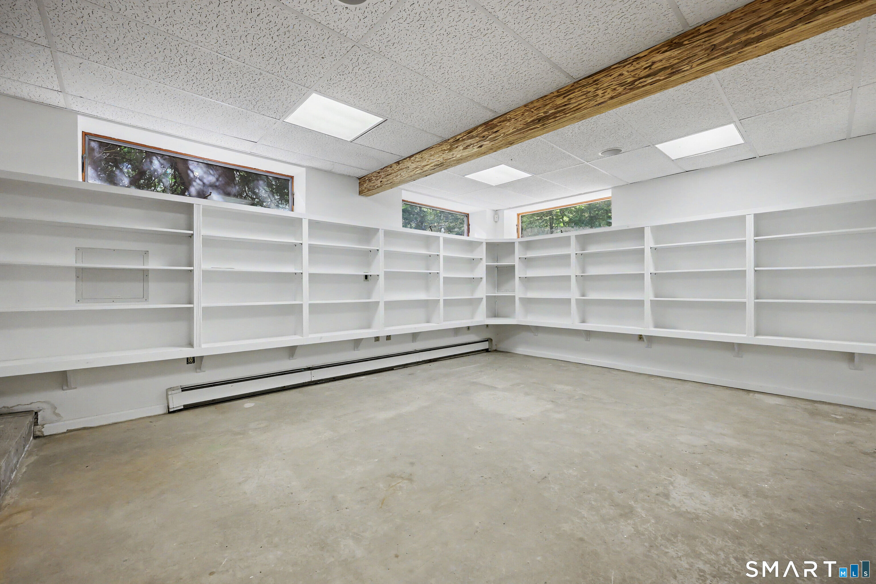 Empty room with built-in white shelves, a concrete floor, and an exposed wooden beam.
