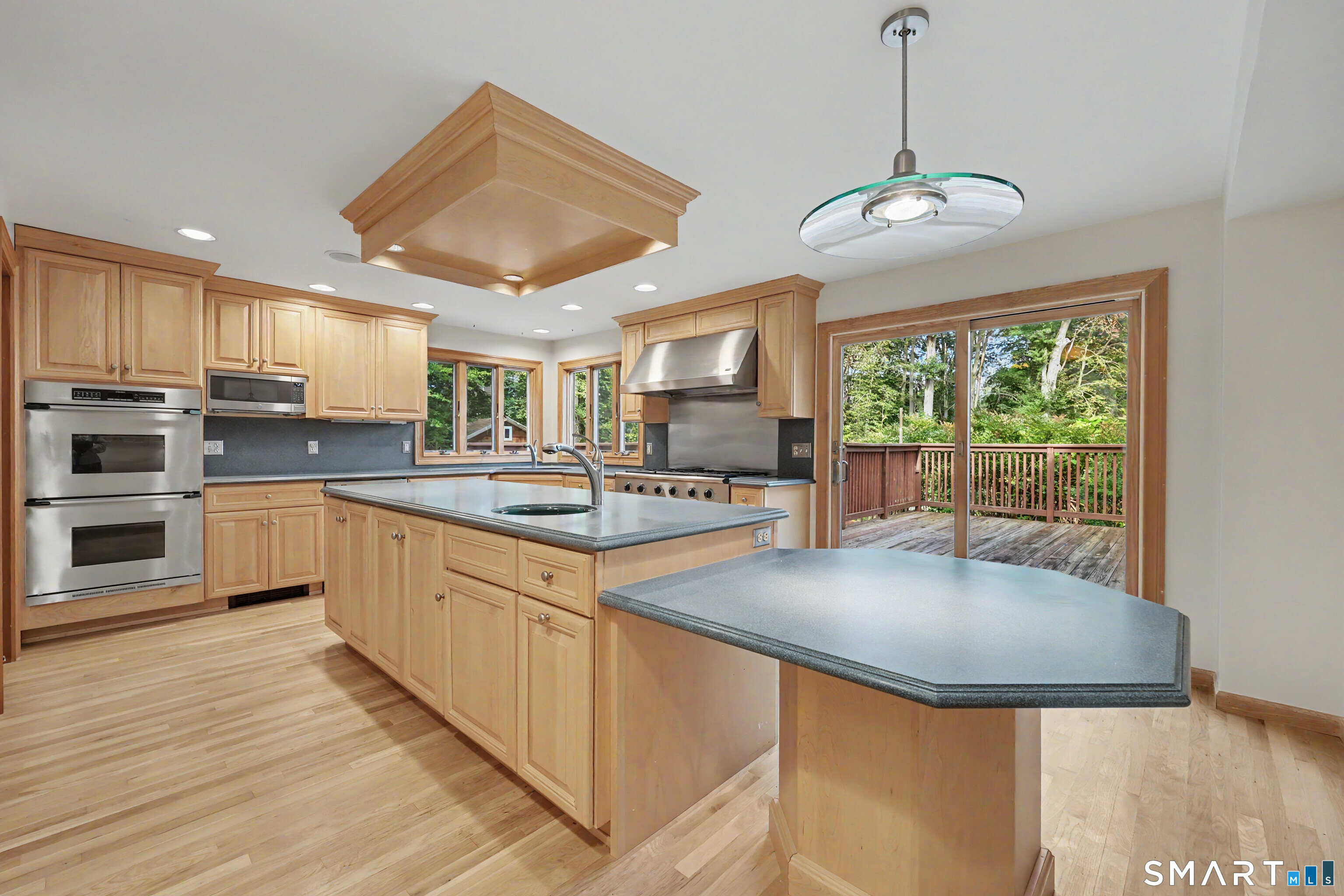 Kitchen with wood cabinetry, a large island, double ovens, and sliding doors to a wooded deck.