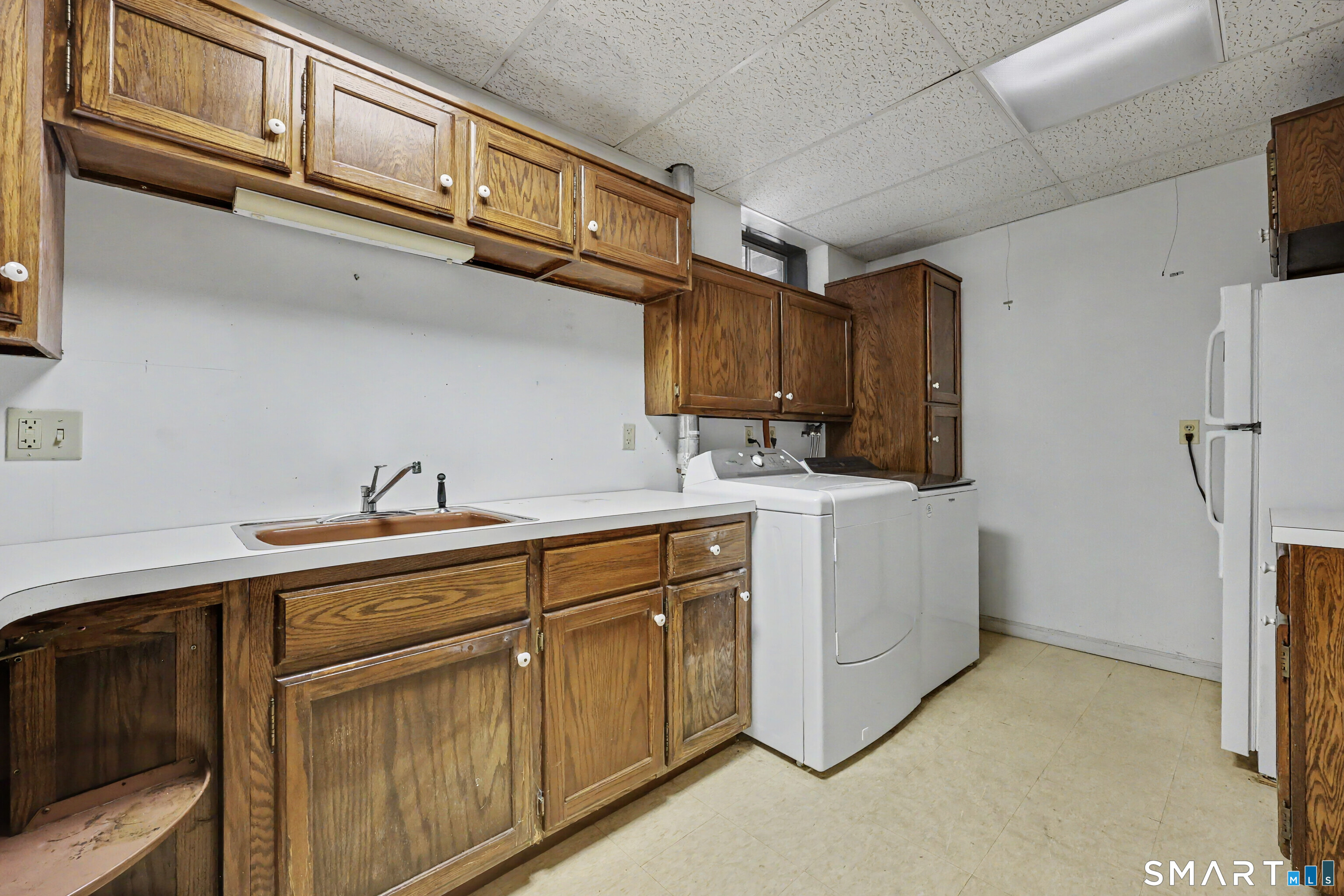Laundry room with a deep sink, wood cabinets, washer and dryer, and refrigerator.
