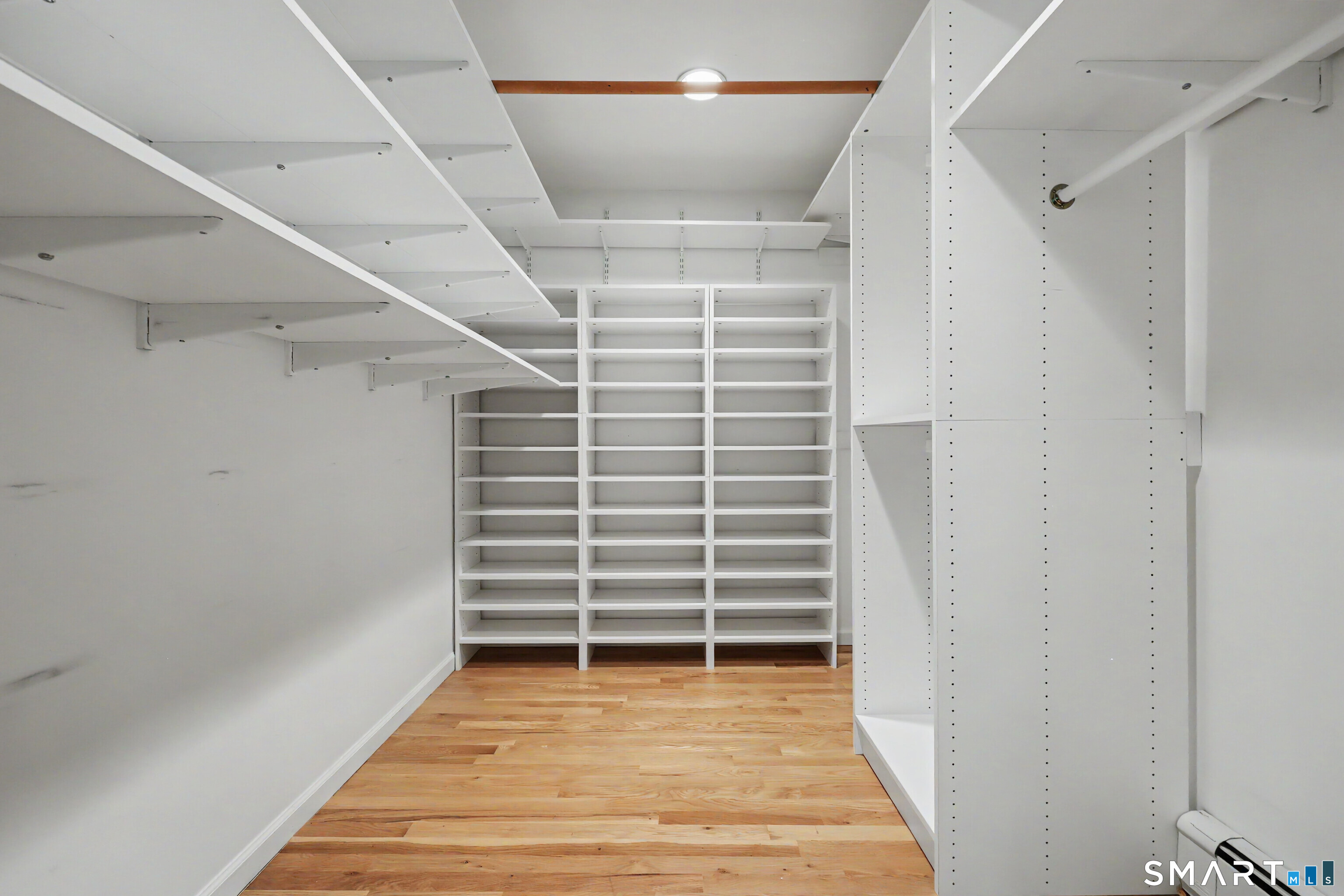 Walk-in closet with extensive white built-in shelving and warm wood flooring.