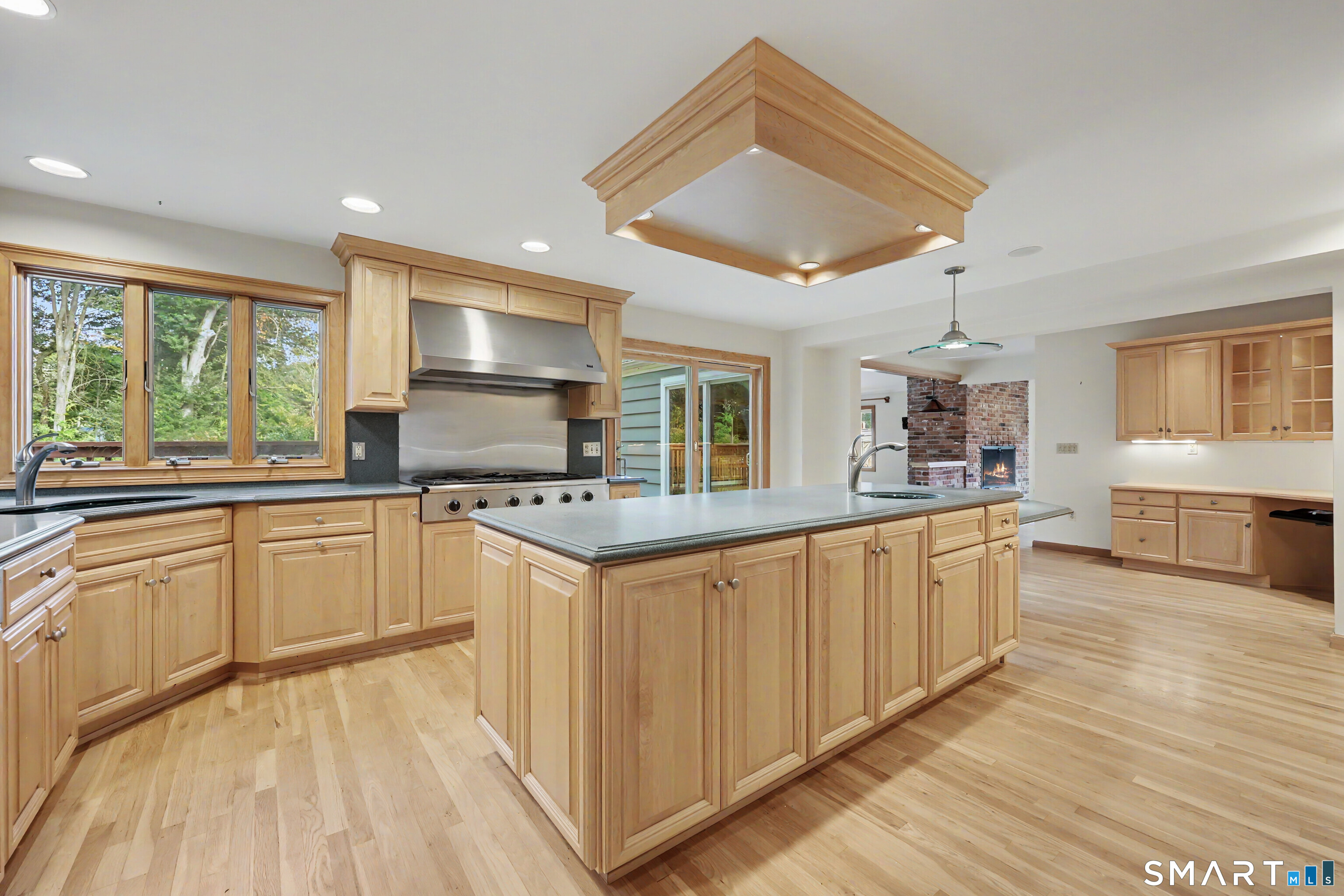 Kitchen with a large wood-cabinet island, stainless steel range, and windows overlooking trees.