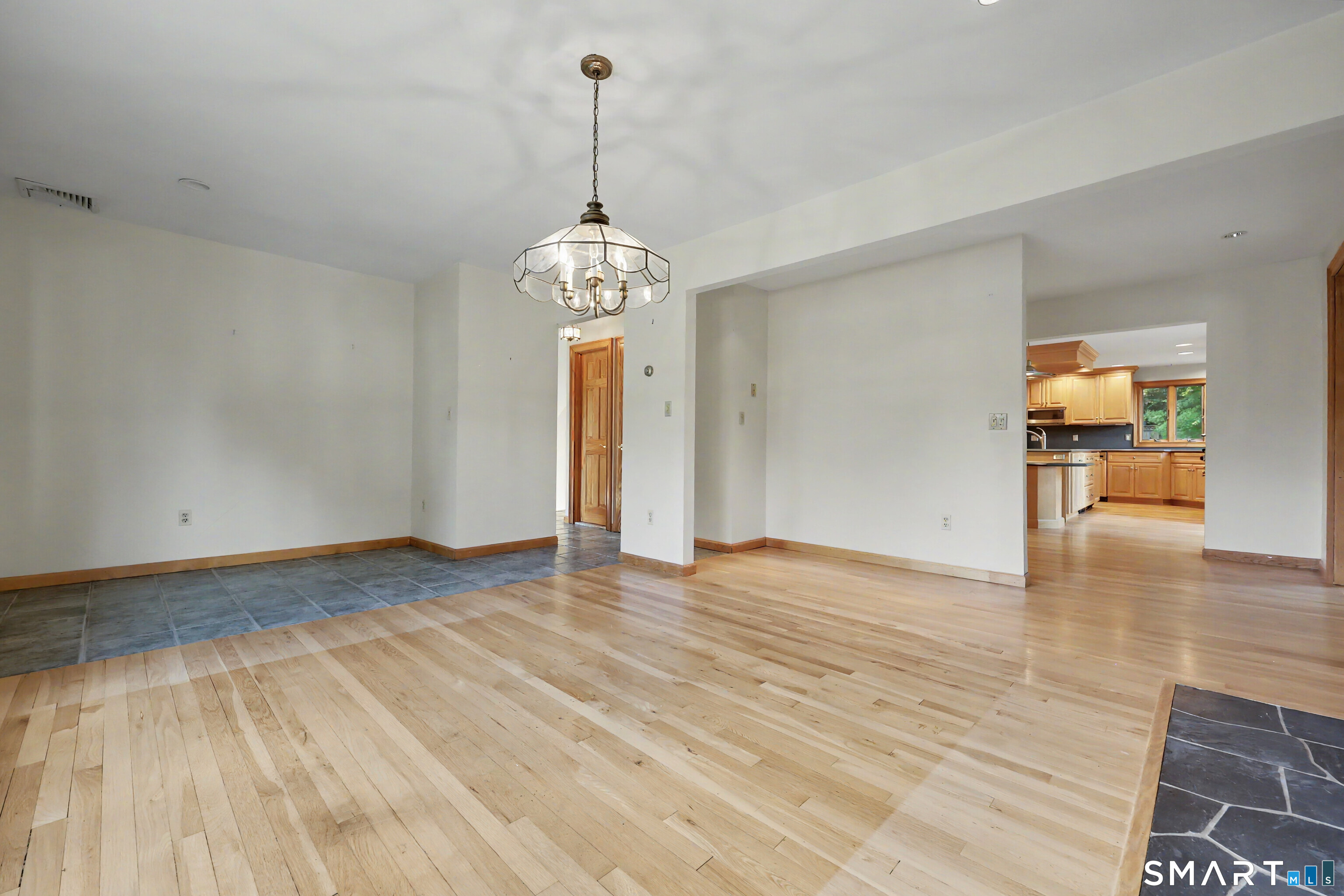 Empty dining area with hardwood floors and chandelier, opening to a kitchen with wood cabinets.