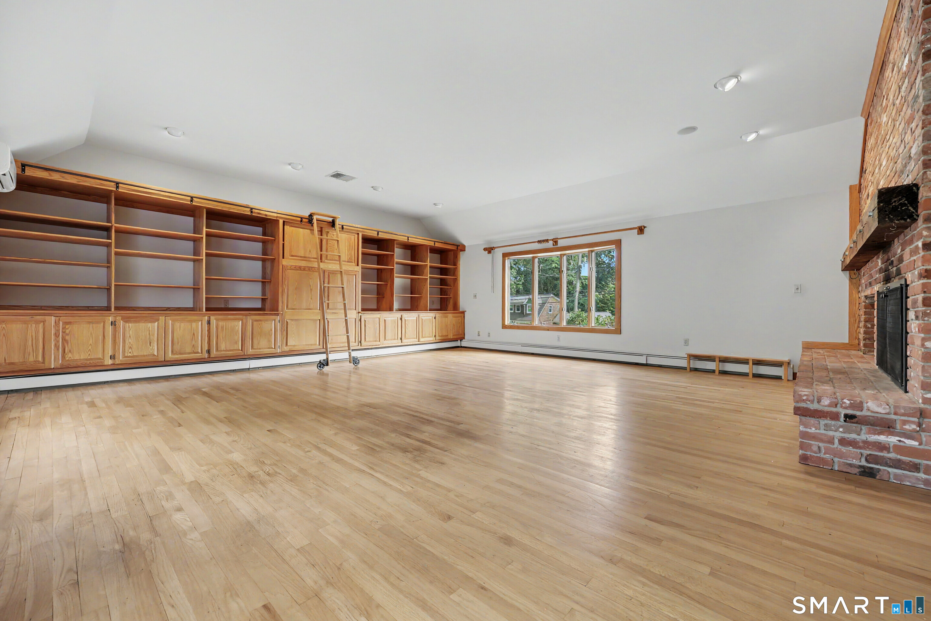 Room with built-in wooden bookshelves, a rolling ladder, hardwood floors, and a brick fireplace.