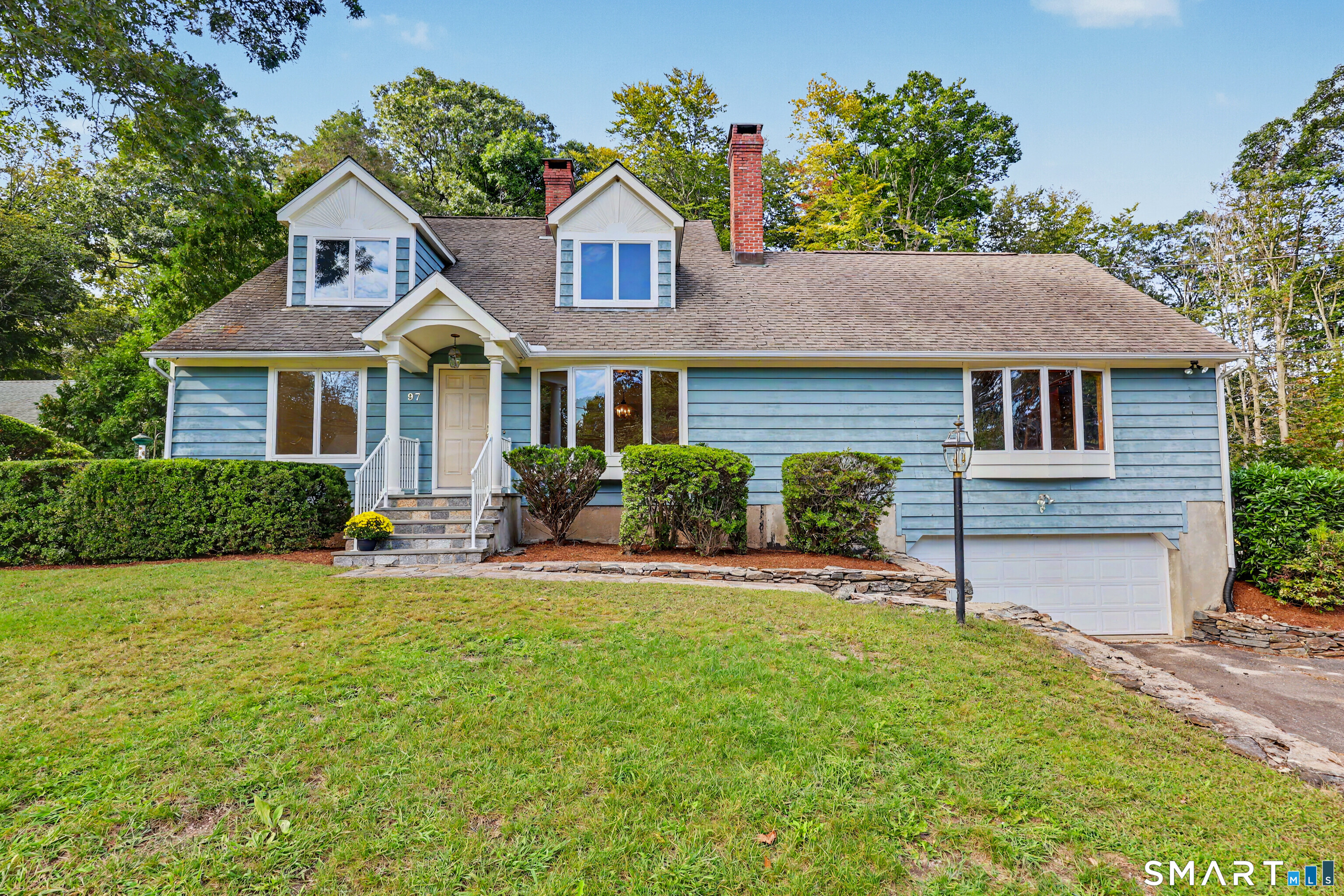 Blue-sided Fairfield home with two dormers, a brick chimney, front porch, and attached garage.
