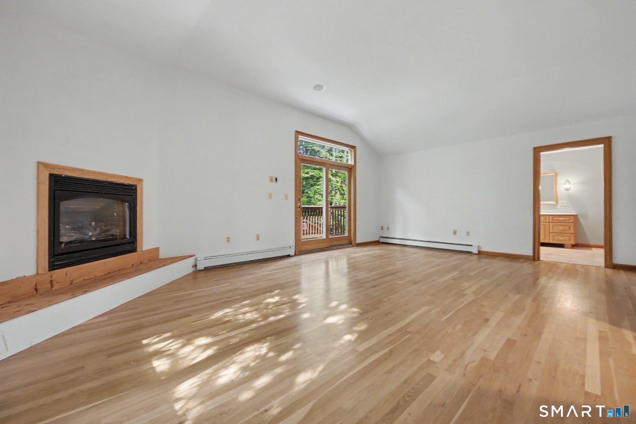 Vacant living room with hardwood floors, a wood-trimmed fireplace, and glass doors to a deck.