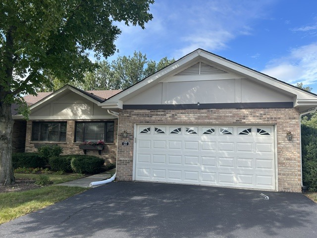 Brick home with a wide white garage door and mature tree beside the driveway.