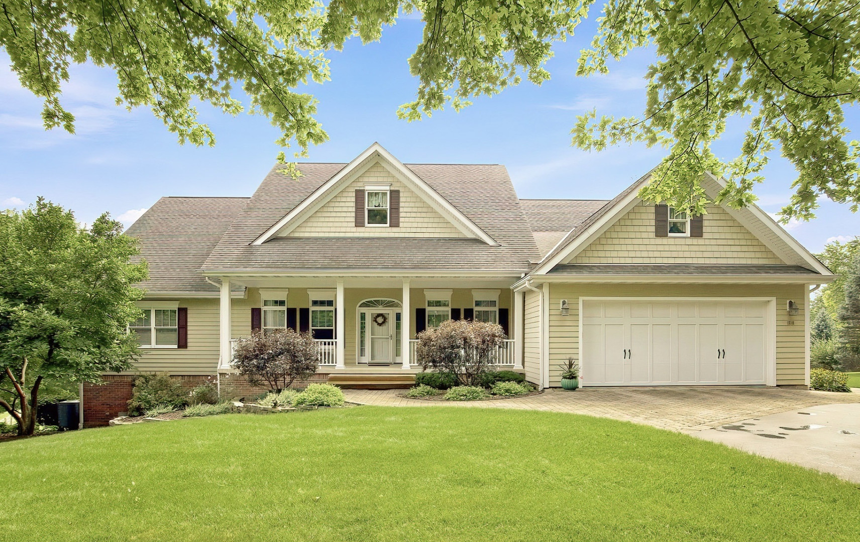 Beige gabled home with a covered front porch, double garage, and leafy trees.