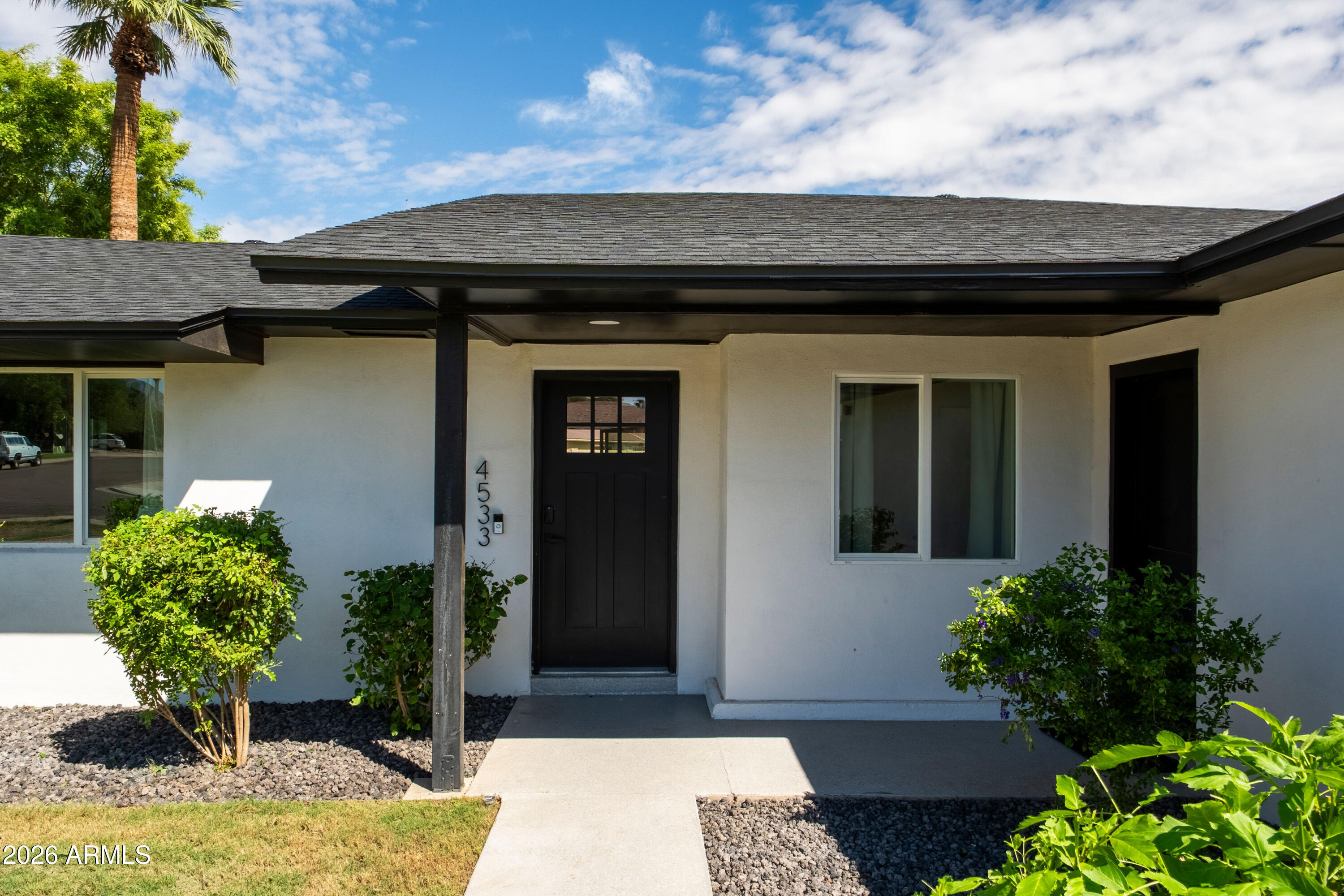 Single-story white stucco home with a black front door, covered entry, and landscaped gravel beds.
