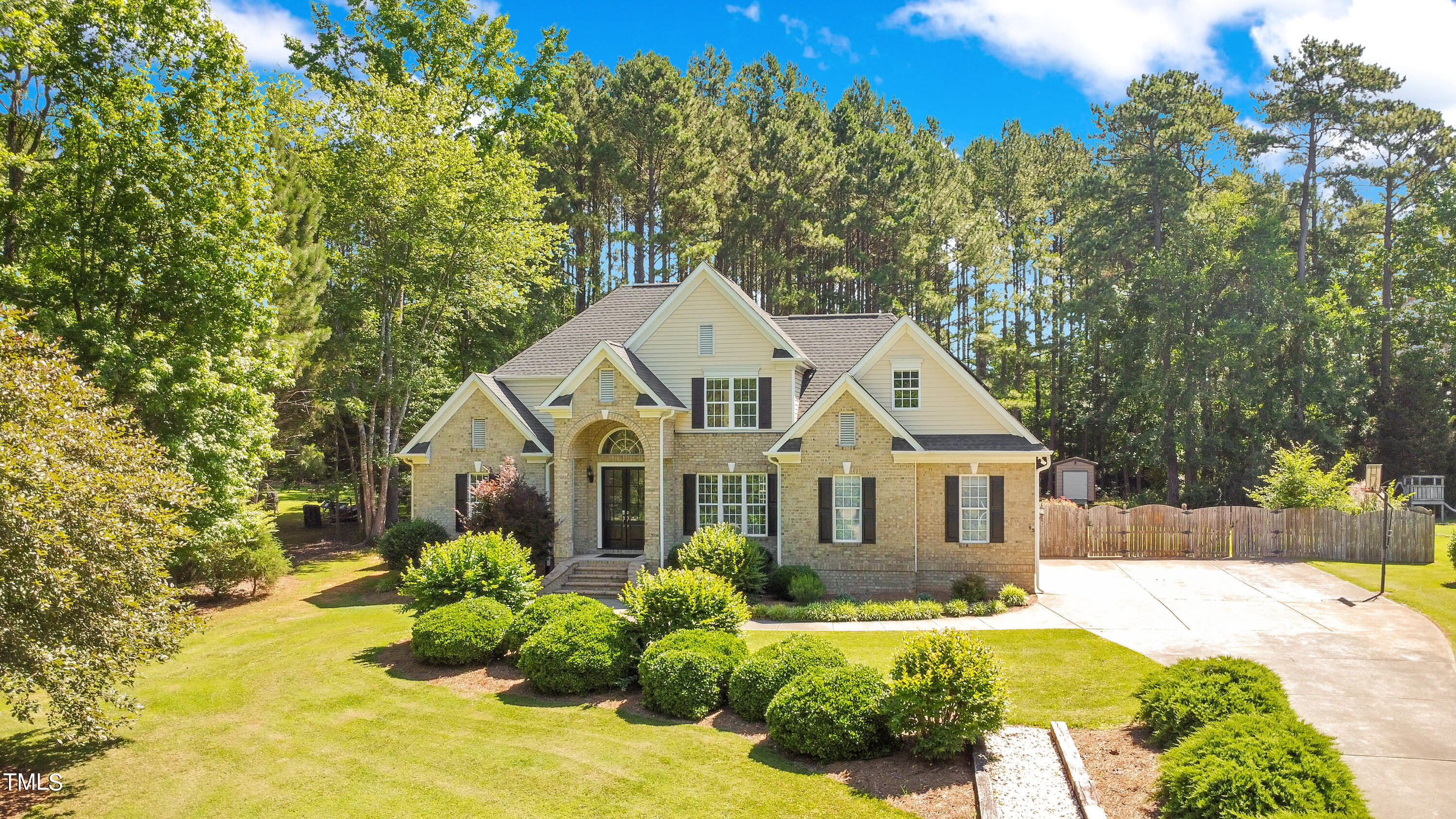Two-story brick house with pale siding, landscaped shrubs, and a broad driveway