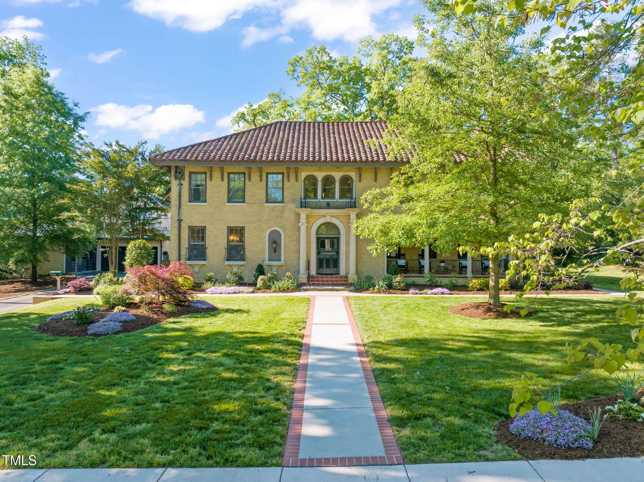 Yellow-brick home with a red tile roof, arched entry, and landscaped front lawn.