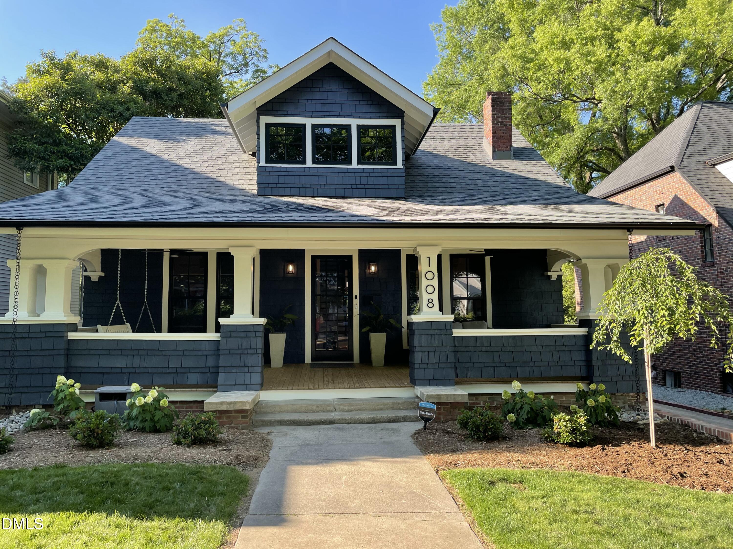 Dark shingle house with white-trimmed covered porch, hanging swing, and front walkway.