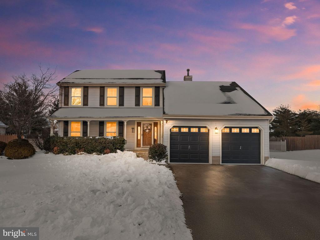 Two-story house with a two-car garage and snow-covered roof at dusk, its windows glowing warmly.