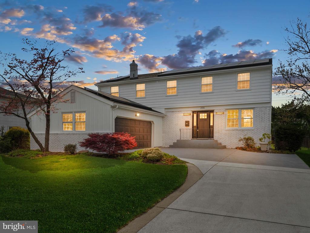 Two-story white house with an attached garage and lit windows at dusk.