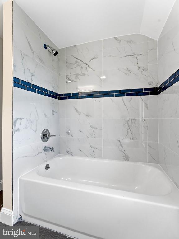 Bathroom tub and shower with marble-look tile, a dark blue accent band, and chrome fixtures.