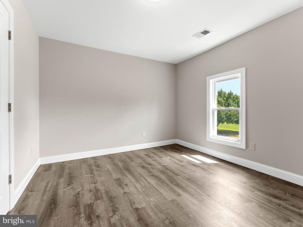 Empty room with wood-look flooring and a window overlooking a green lawn and trees.