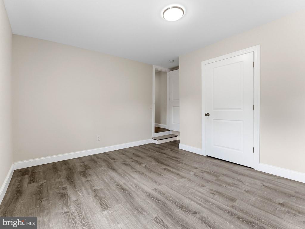 Empty room with gray wood-look flooring, pale walls, and a white paneled door.