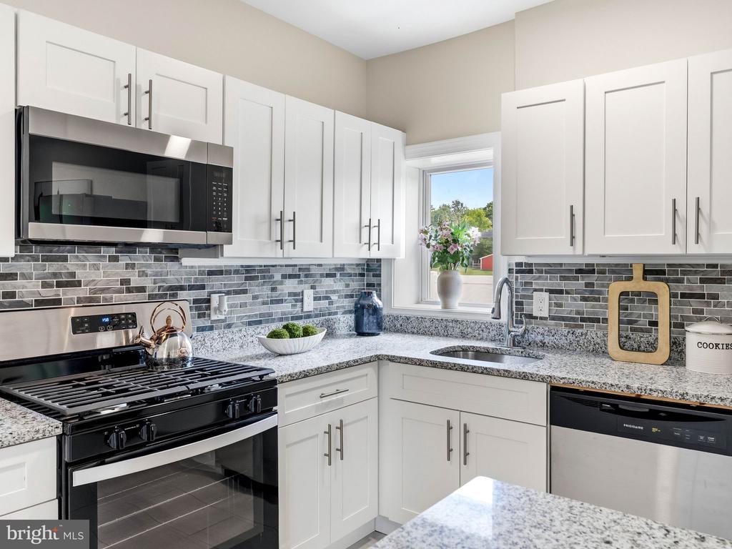 Kitchen with white shaker cabinets, granite counters, gray mosaic backsplash, and black range.