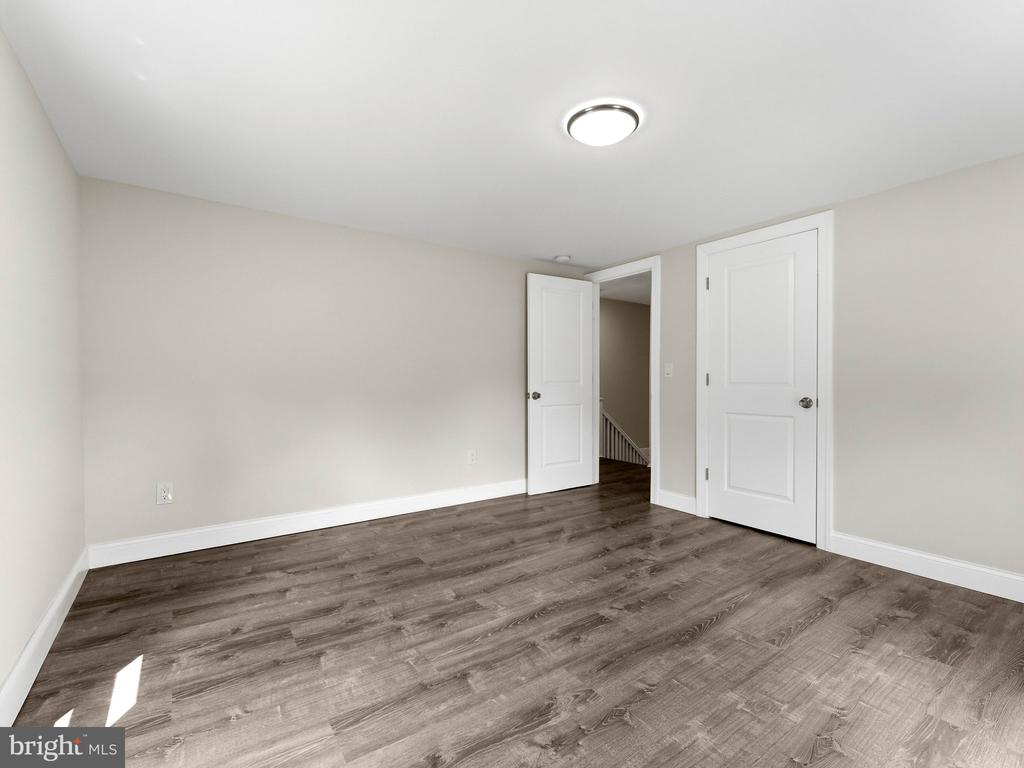 Vacant bedroom with wood-look flooring, white doors, and an open doorway to a staircase.