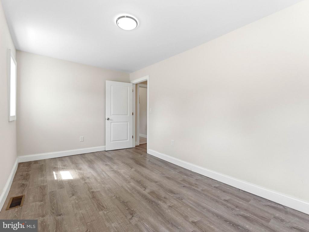 Empty room with gray wood-look flooring, white walls, and an open door.