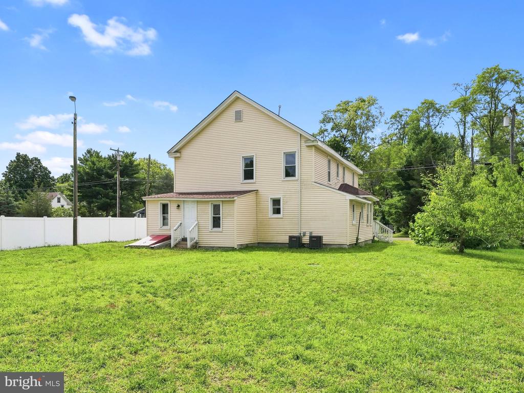 Two-story beige-sided house with a broad grassy yard, white fence, and small ramp.