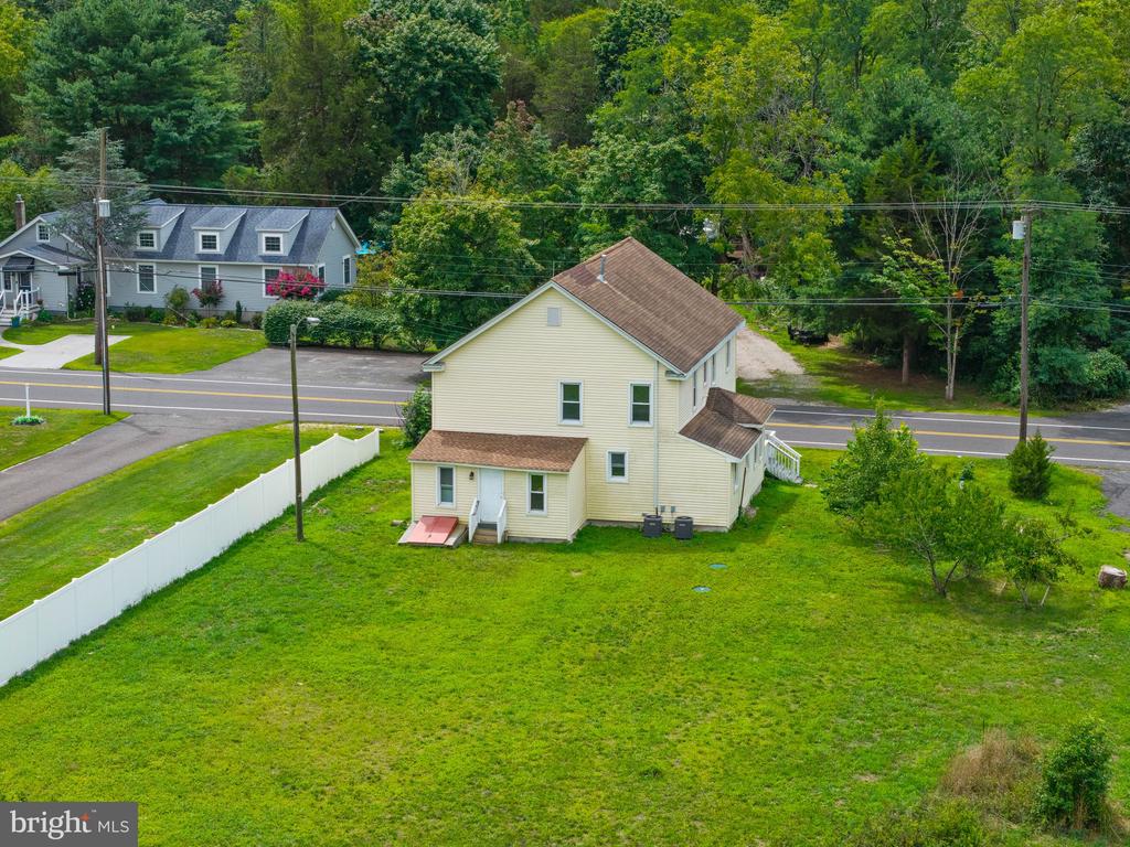 Aerial view of a pale yellow house with a large grassy yard and white fence beside Route 542.