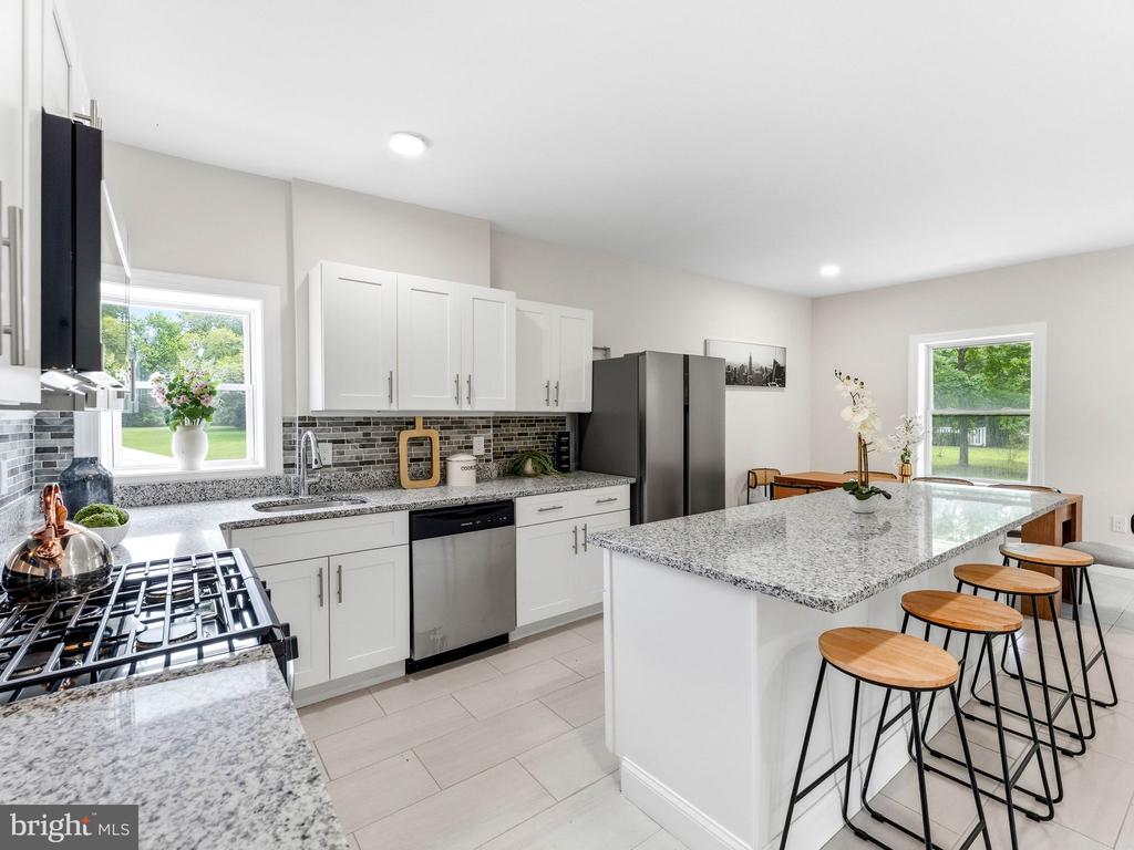 Bright kitchen with white cabinets, stainless steel appliances, and a large granite island with stools.