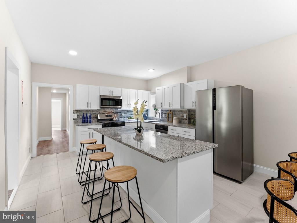 Renovated kitchen with a large granite island, white cabinets, and stainless steel appliances.