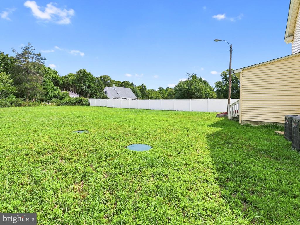 Grassy backyard bordered by a white privacy fence beside the yellow-sided house.