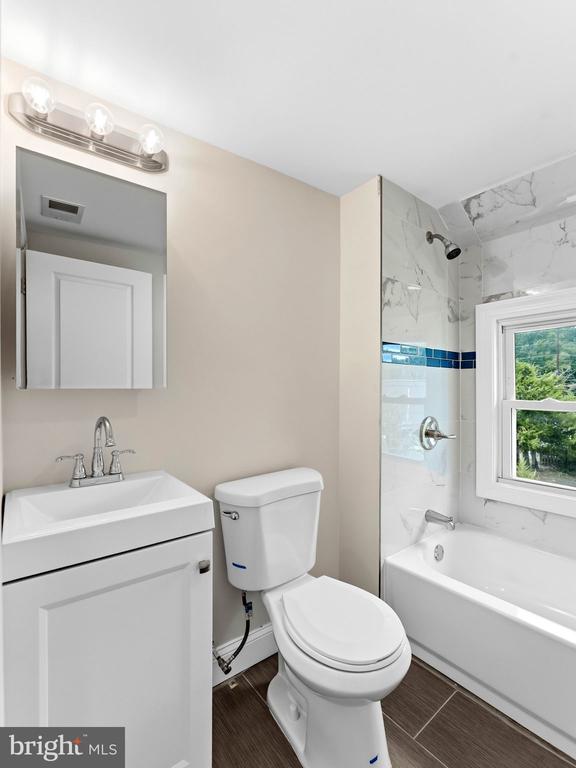 Bathroom with white vanity, toilet, and tub featuring marble-look tile and a blue accent stripe.