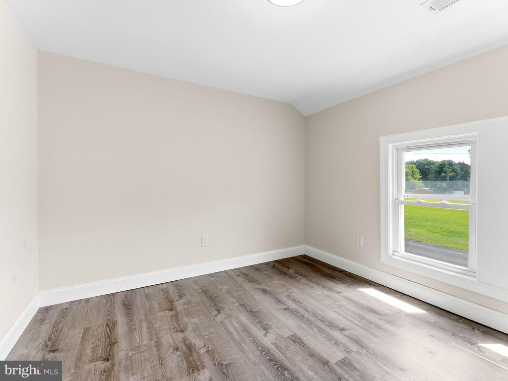 Empty room with gray-brown plank flooring and a window overlooking a lawn.