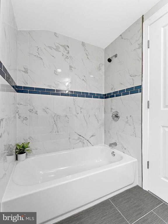 Bathroom with a white tub, marble-look tile, and a dark blue accent band.