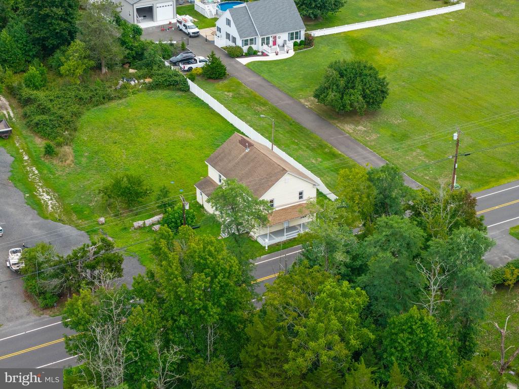 Aerial view of a white house beside a road, with a large lawn, outbuilding, and long driveway.