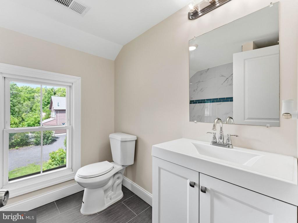Bathroom with a white vanity, toilet, dark tile floor, and a window overlooking greenery.
