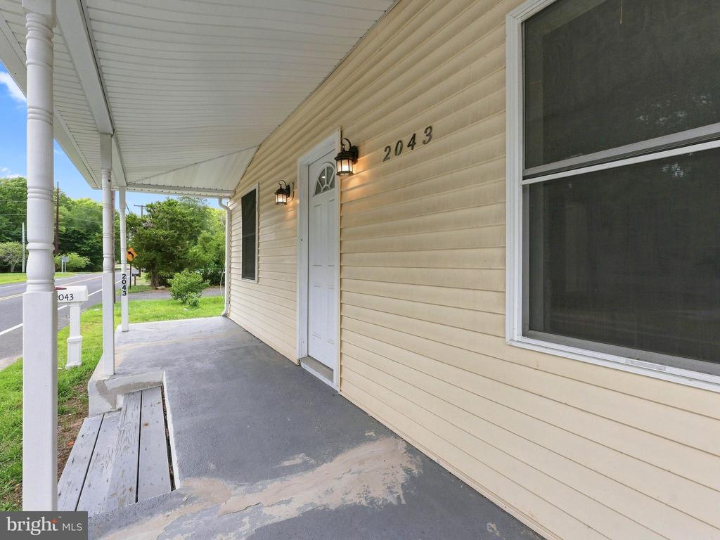 Covered front porch with a white entry door, beige siding, and the number 2043.