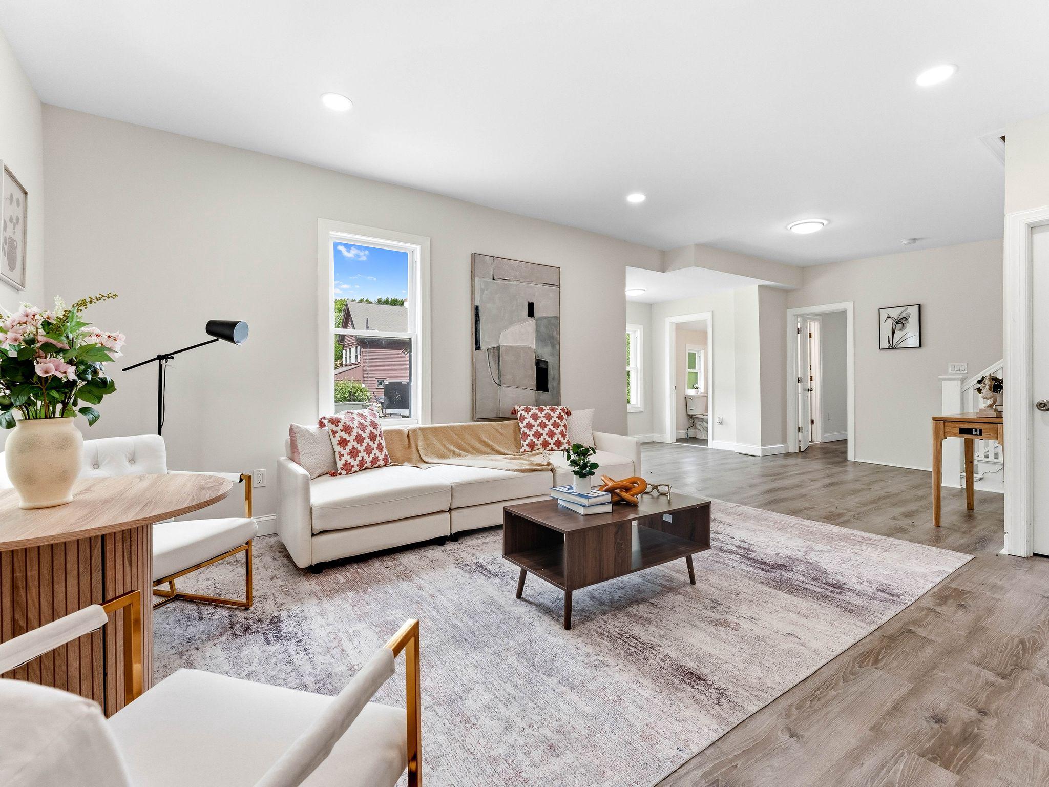 Furnished living room with a white sofa, patterned cushions, and an open hallway.