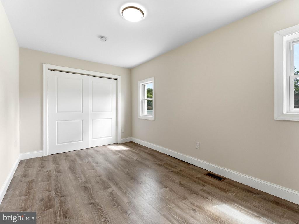 Unfurnished bedroom with white closet doors, wood-look flooring, and two windows.