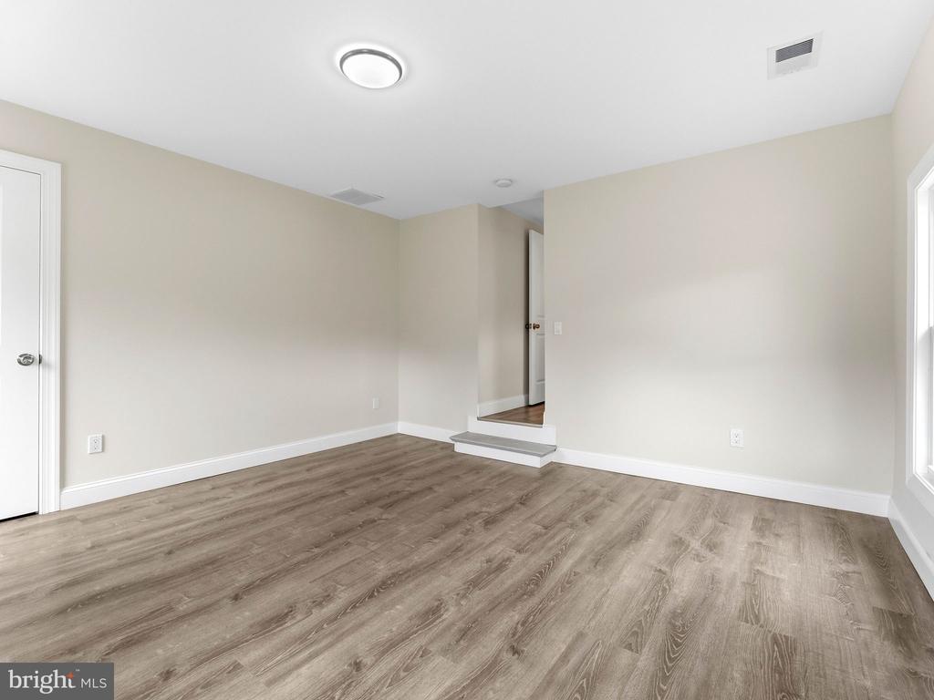 Empty room with wood-look flooring, beige walls, and a raised doorway opening.