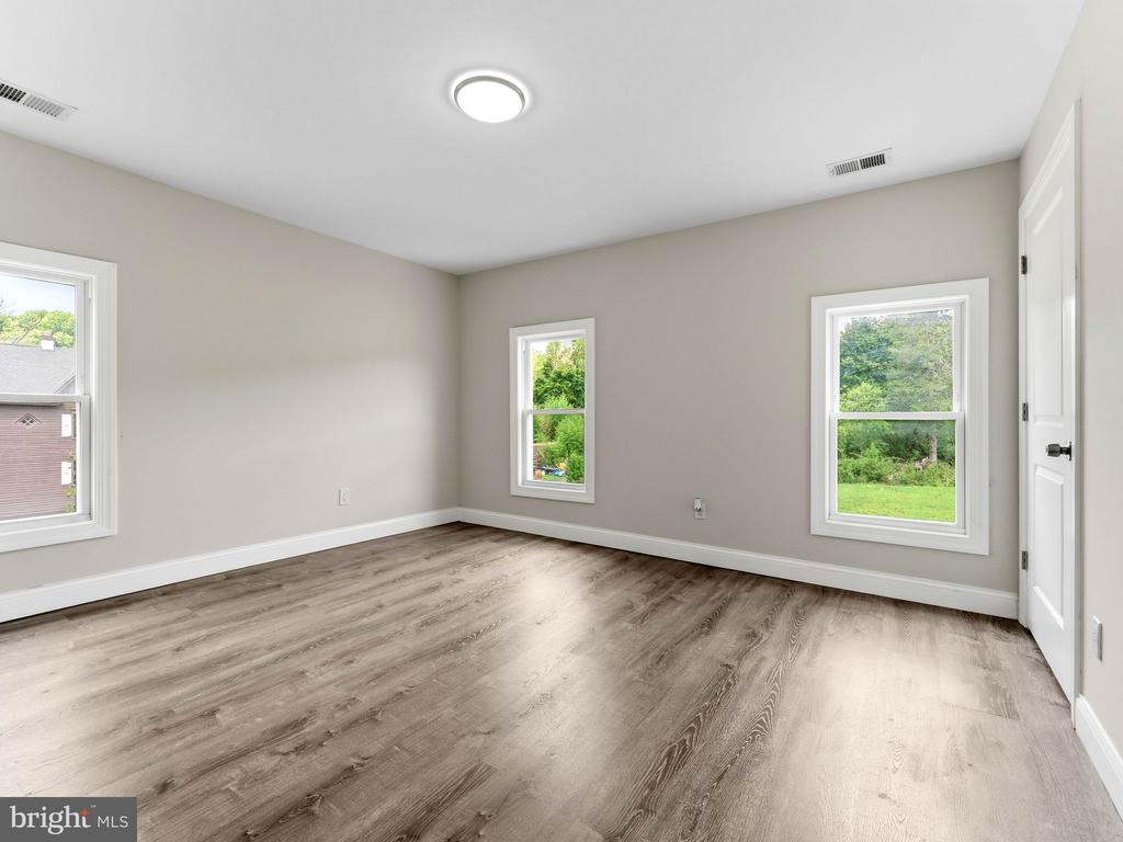 Vacant room with wide-plank flooring, three windows, and a recessed ceiling light.