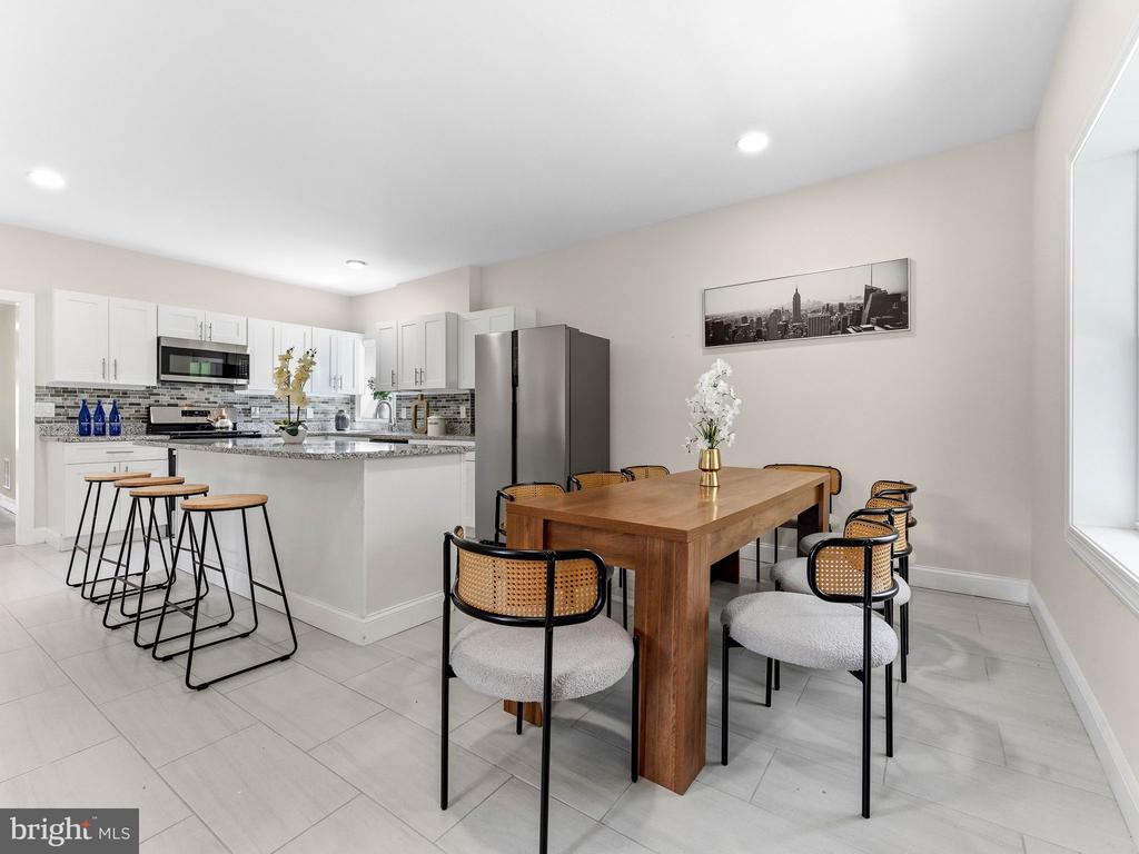 Open kitchen and dining area with white cabinets, breakfast bar stools, and a wooden dining table.