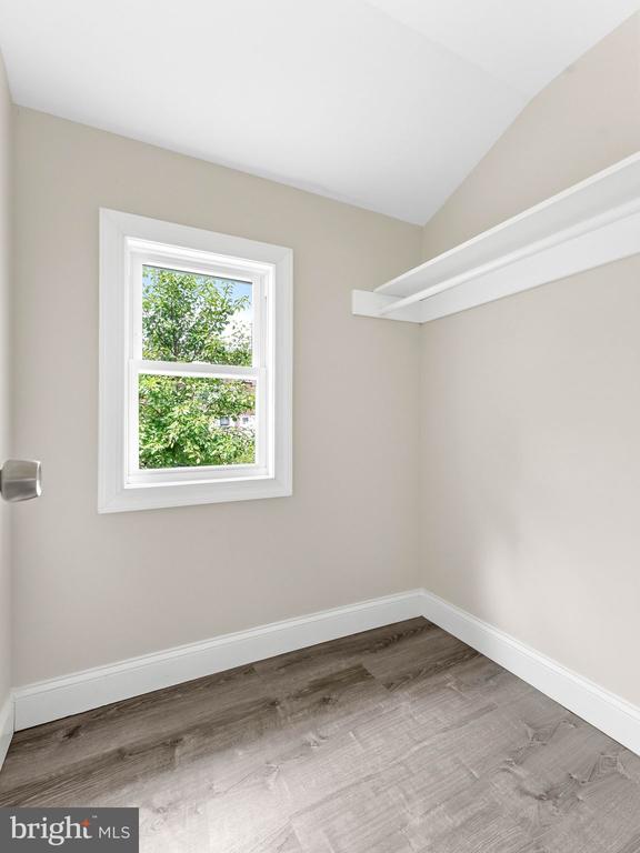 Empty closet with a window, a white upper shelf, and gray-brown wood-look flooring.
