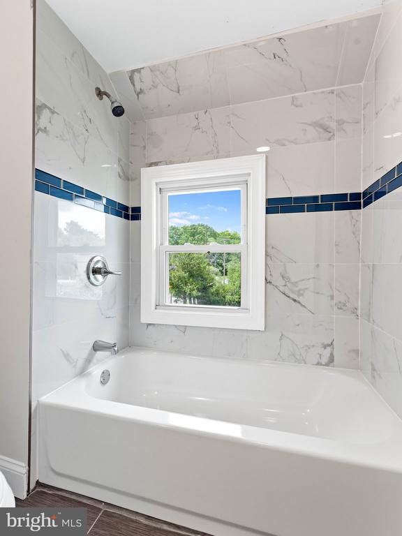Bathroom with a white bathtub, marble-look tile, blue accent band, and window.