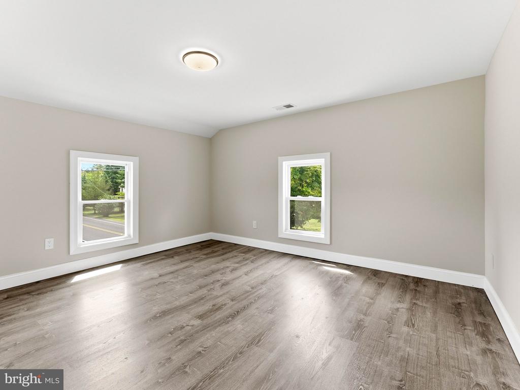 Empty room with gray-brown plank flooring, neutral walls, and two windows overlooking greenery.