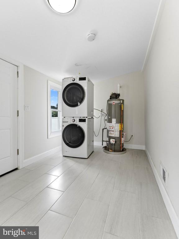 Laundry room with stacked front-loading washer and dryer beside a water heater.