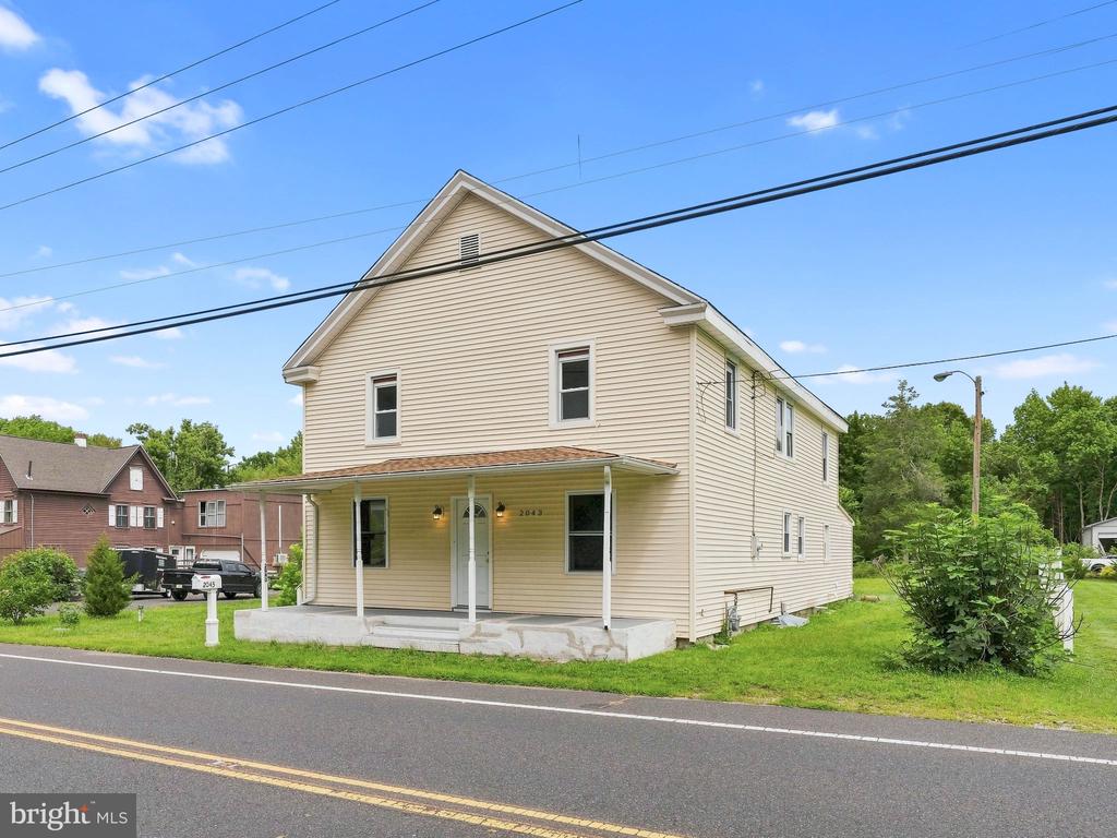 Two-story beige house with a covered porch beside a road.