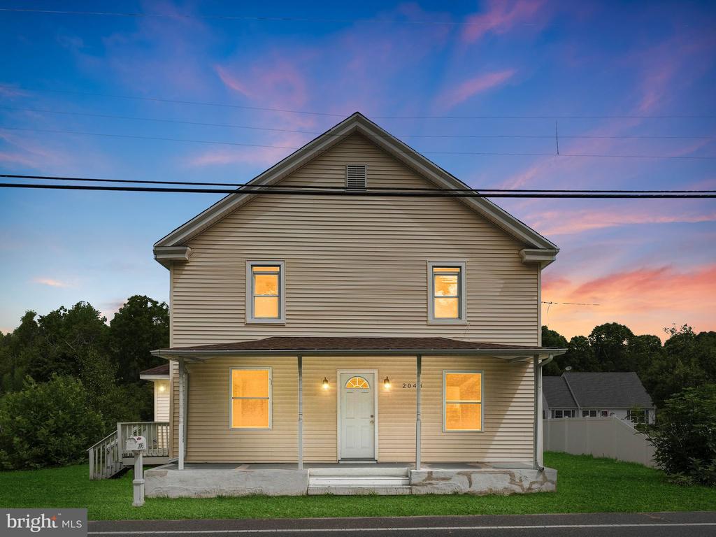 Two-story beige house with a covered porch and warmly lit windows at dusk.
