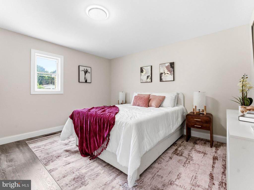 Staged bedroom with a white bed, burgundy throw, pink pillows, and pale patterned rug.