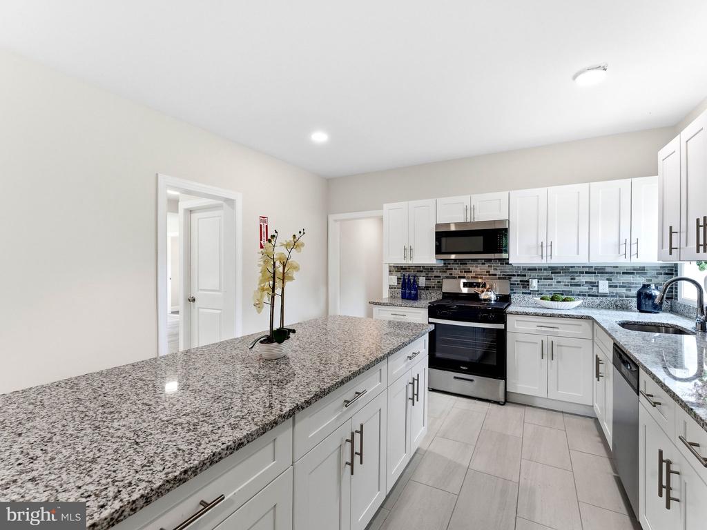 Kitchen with white cabinets, granite island, gray tile backsplash, and stainless steel appliances.