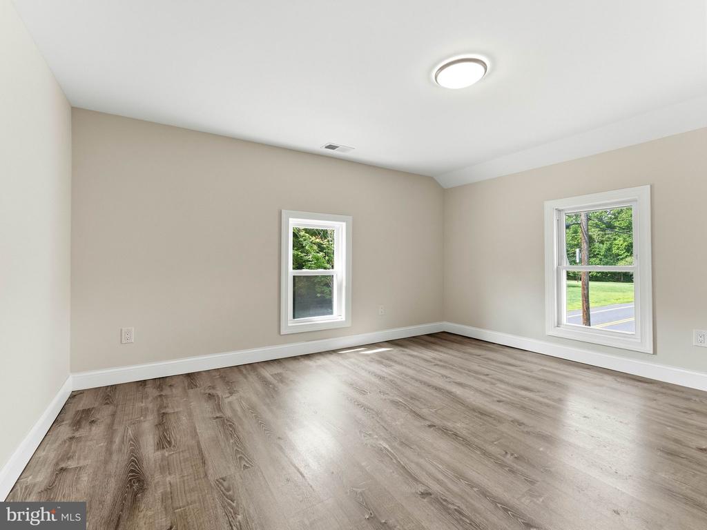 Empty room with wood-look flooring, beige walls, and two windows overlooking greenery.